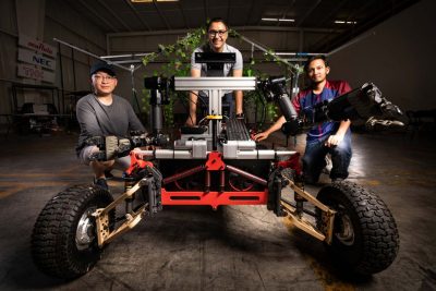 Graduate students pose by their grape harvesting robot in a warehouse.