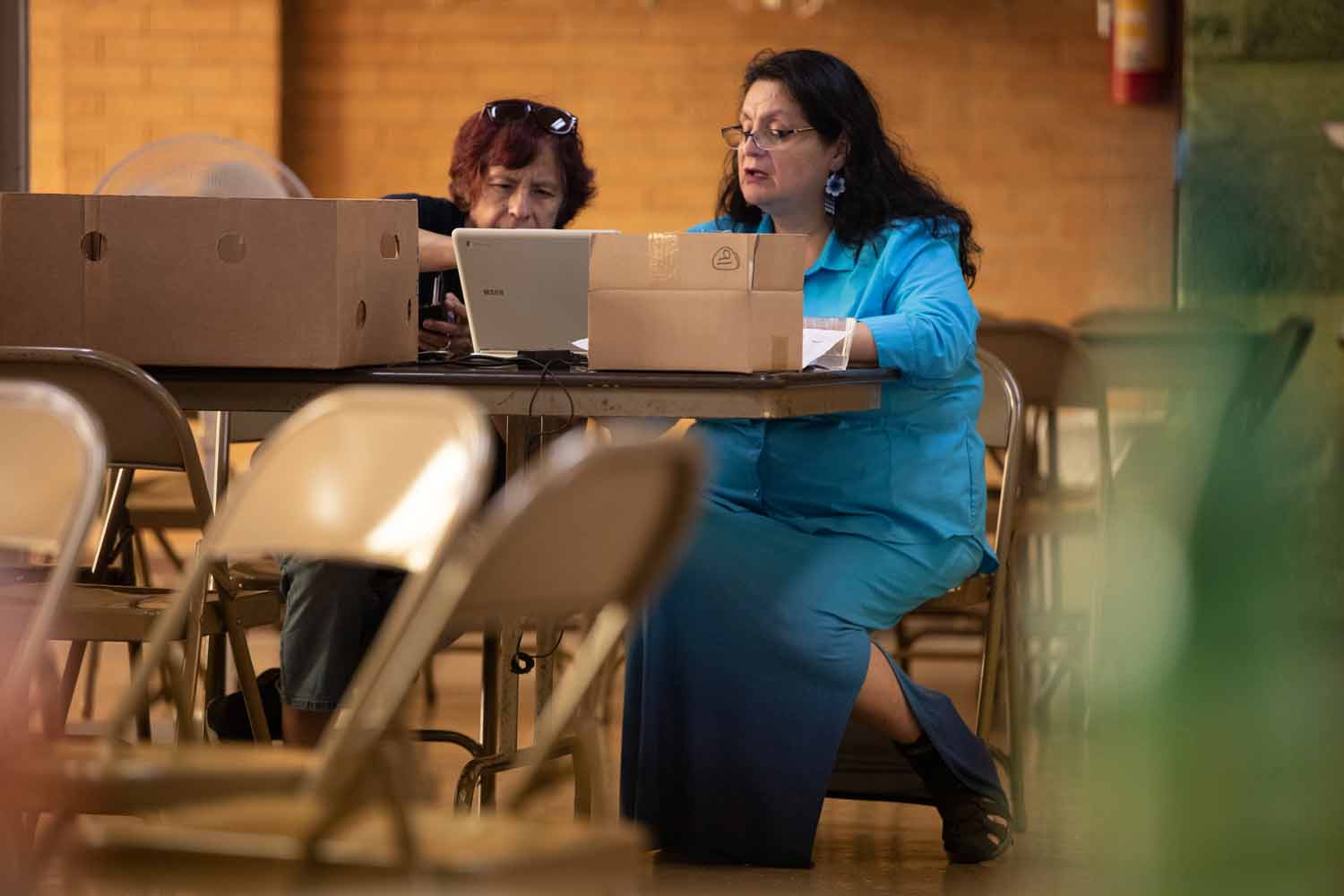 Delia Barajas works on a laptop in a church basement with a volunteer.
