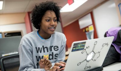 Student smiling at her laptop in a classroom