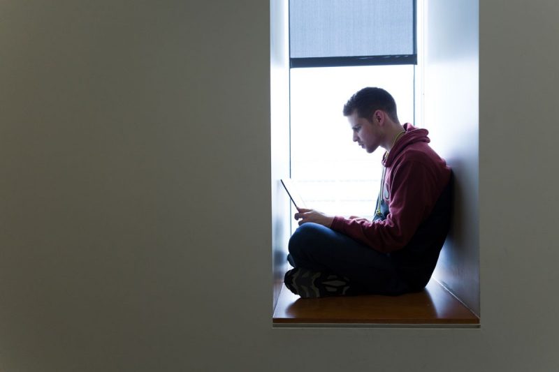Male student on his laptop sitting in a window.