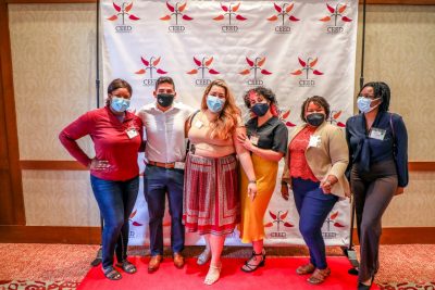 Six Graduate Students posing together with masks on in front of the CEED backdrop and on a red carpet