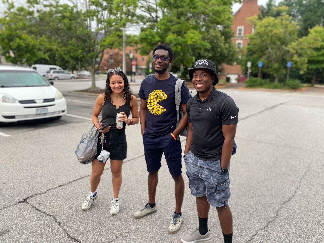 three students pose together and smile at the camera in a parking lot