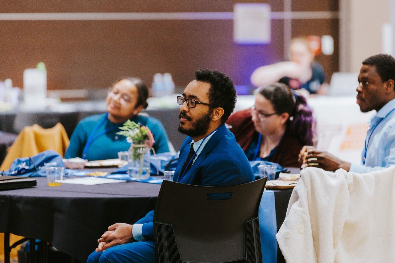 Graduate student, Alazar Izkinder, sitting a table with other grad students at a conference