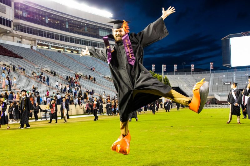 A student jumping at commencement with HokieBird feet.