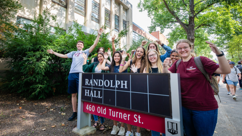 Students stand around the Randolph Hall sign smiling