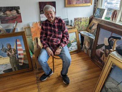 Terry Lyon in his studio, alongside a recent series of paintings of his father with his World War II plane.
