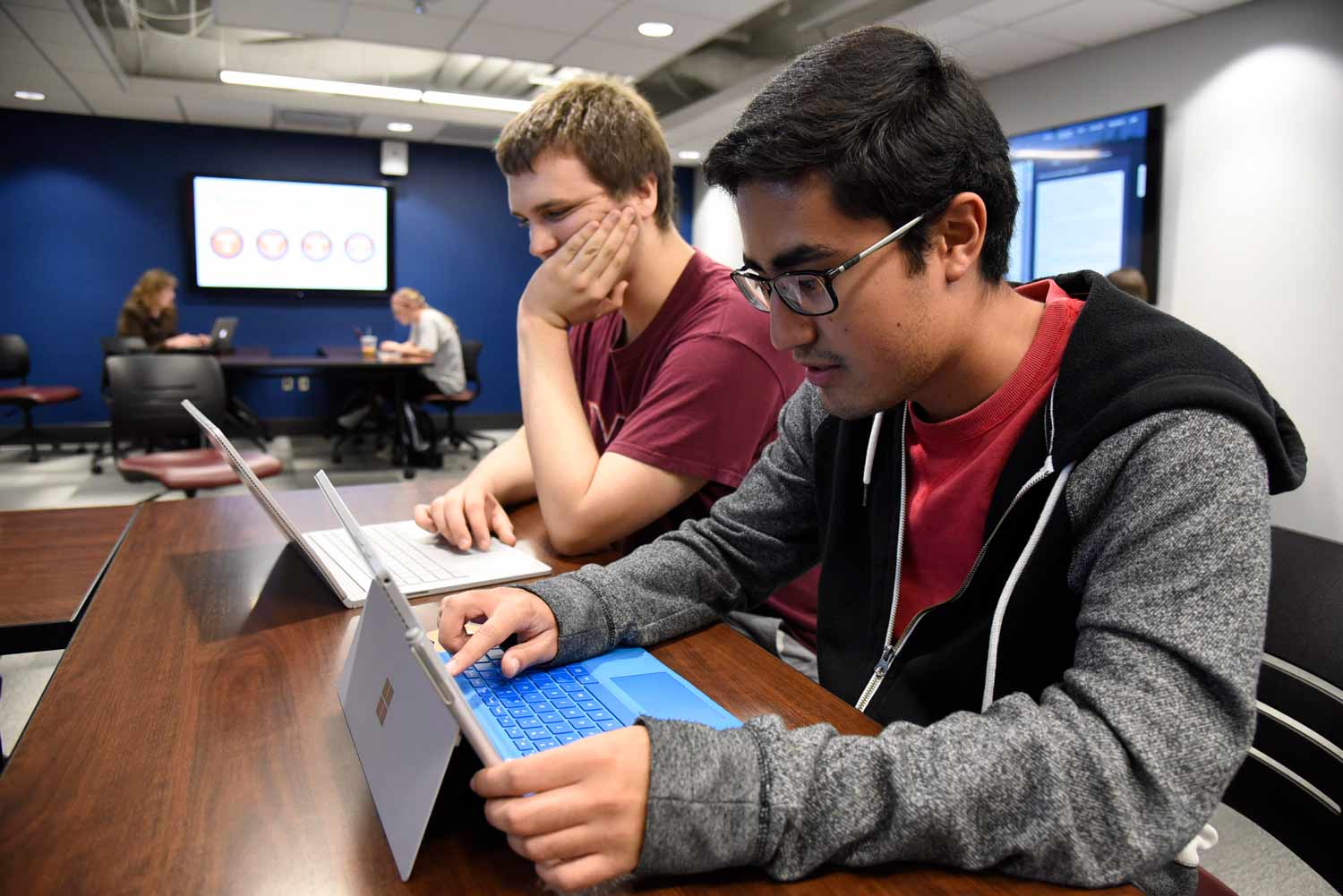 Two Virginia Tech students working on their laptops in a multi-purpose room.