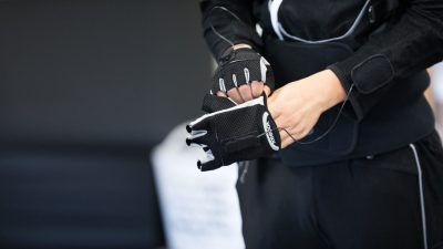 Close up of hands as a person in the black, and wired motion, suit puts on fingerless gloves that are part of the suit.