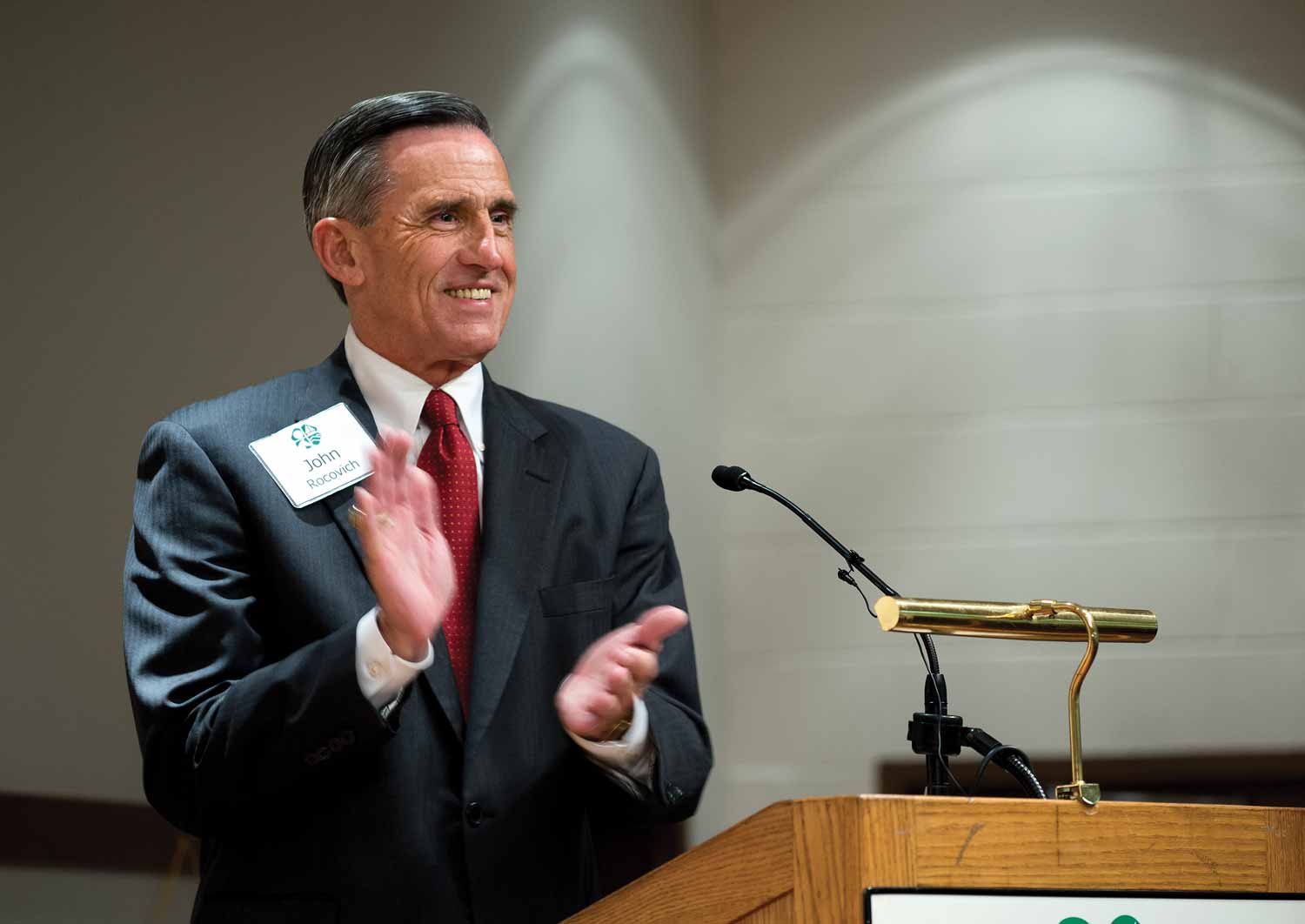 Portrait of John G. Rocovich, Jr., ‘66 Pamplin College of Business, clapping behind a lectern.