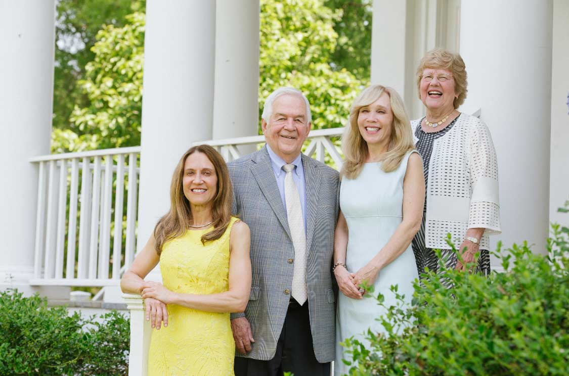 Joe May and his family pose for a group photo in front a grand white porch with green bushes.
