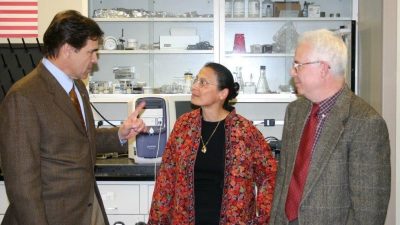 Three people stand talking to each other in a lab.