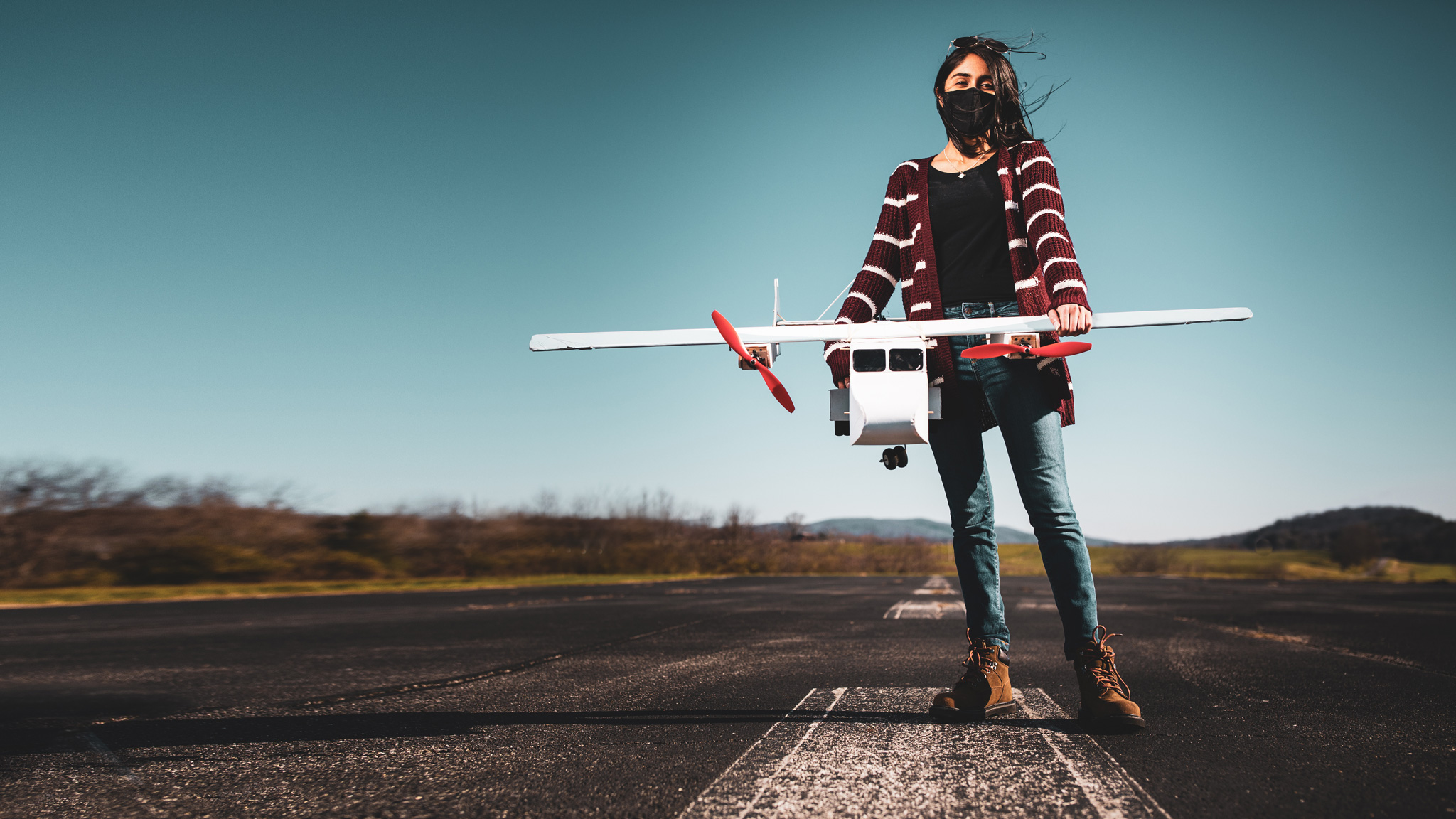 A Design Build Fly team member stands on the tarmac holding a remote control plane.
