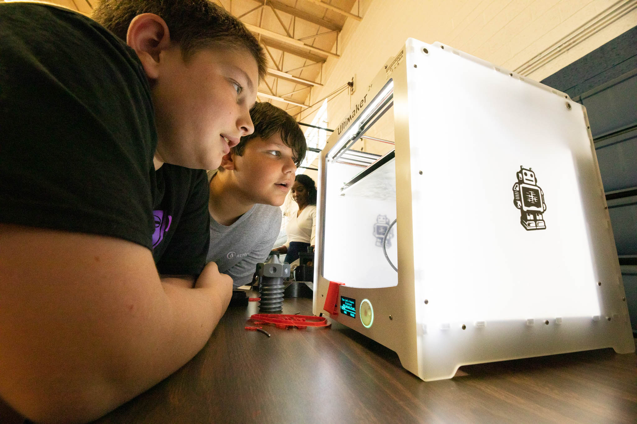 Two young boy students get up close to look at a 3D printer in action.