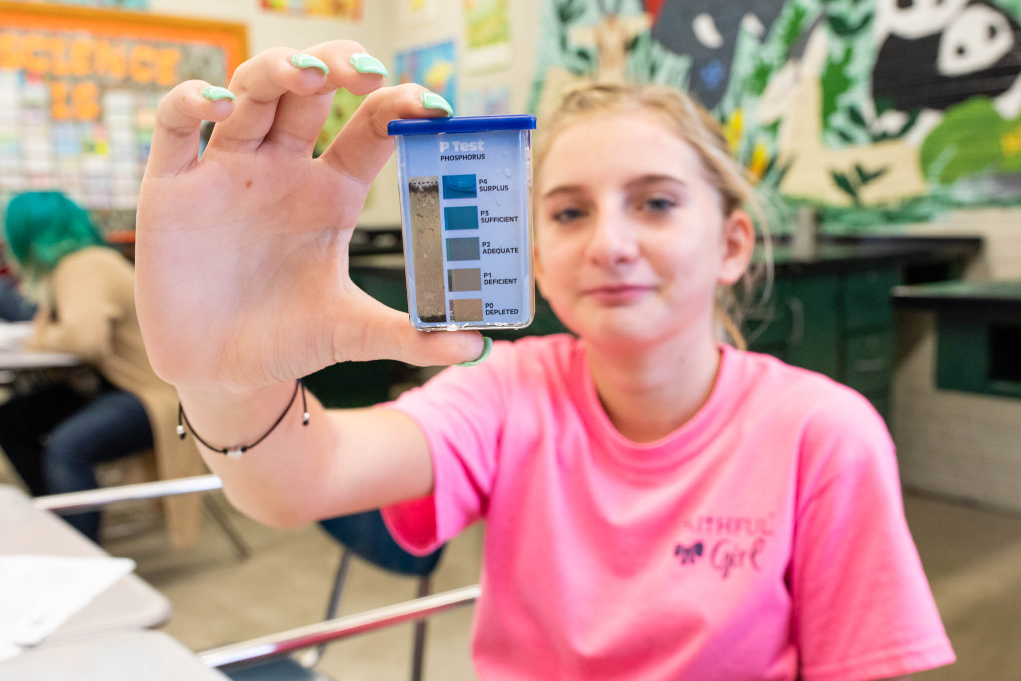 A young female student holds up a water testing plastic container for the camera.