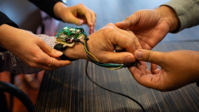 Two sets of hands help put on the wearable haptic wrist unit.