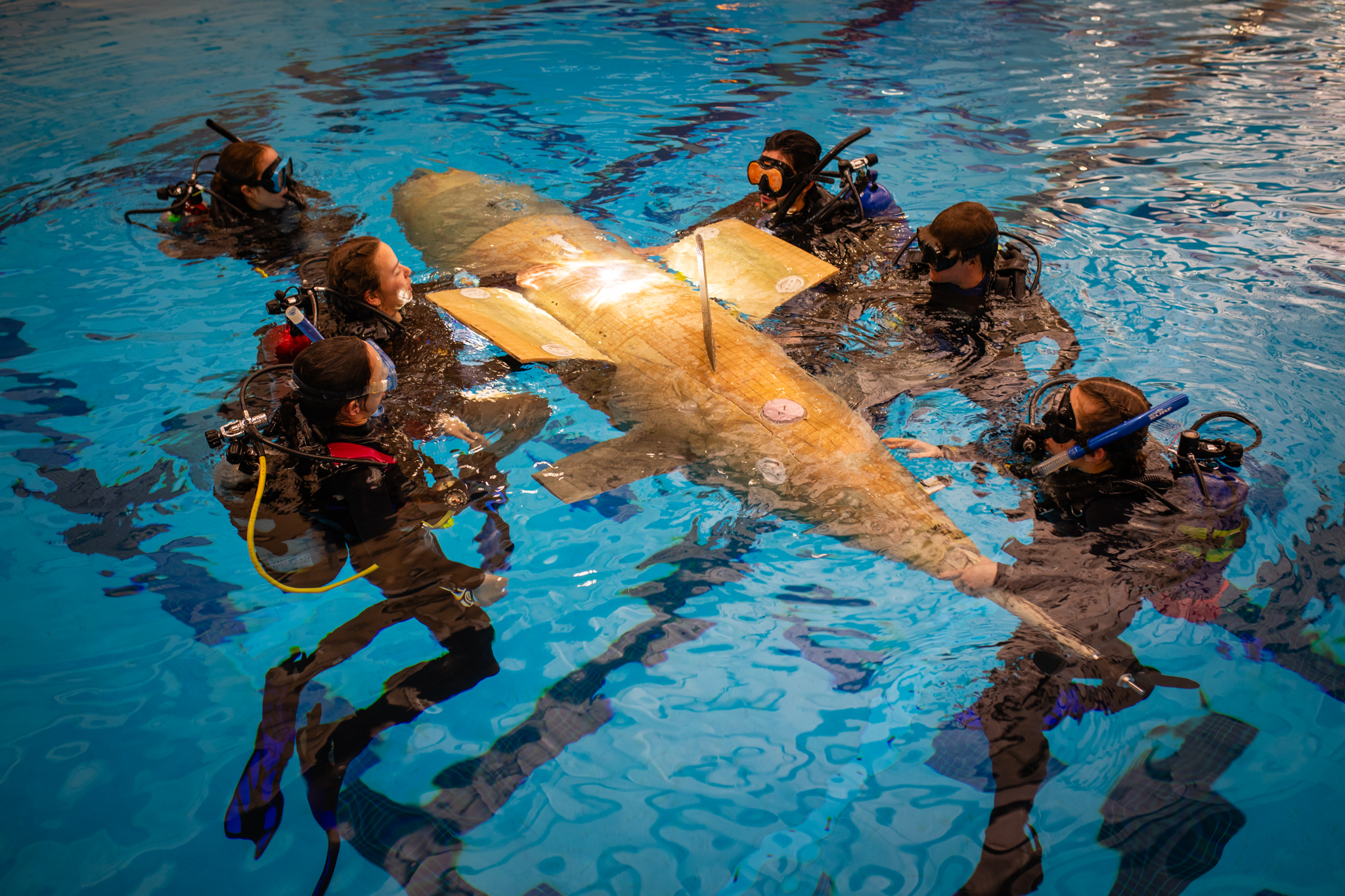 A group of students in scuba gear in a pool surround the sub.