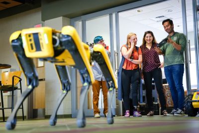 Robotic dog, spot, stands to the left with robotic researchers viewing from behind.