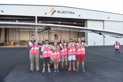 Six Virginia Tech Hokies with the VT hand sign in front of the Electra hangar.