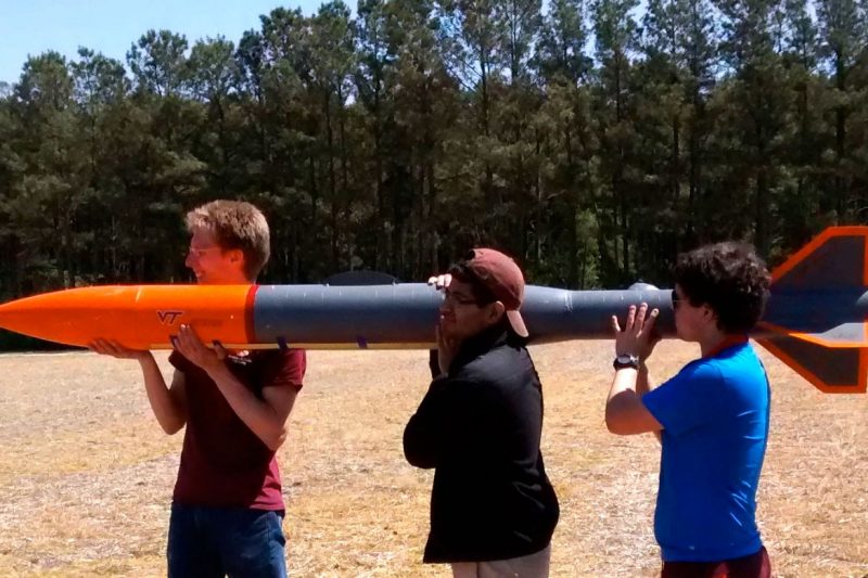 Three students carry a rocket on their shoulders.