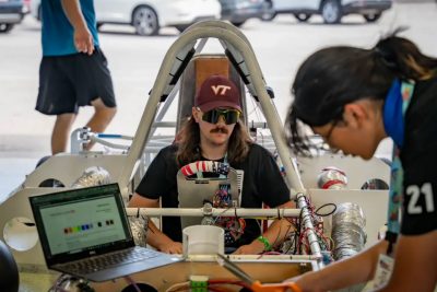 A student works on the open cockpit of the solar car while another student sits in the driver's seat.