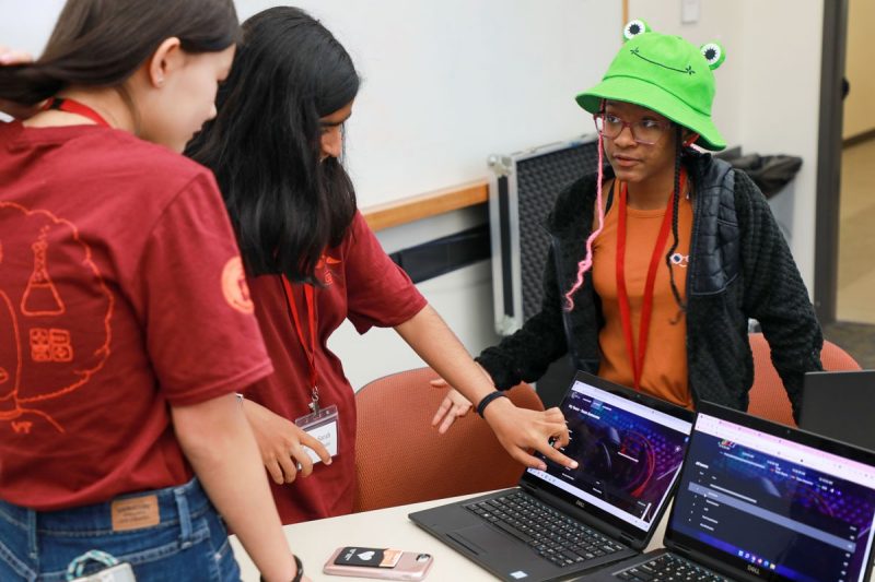 three students stand around two laptops discussing cybersecurity activity