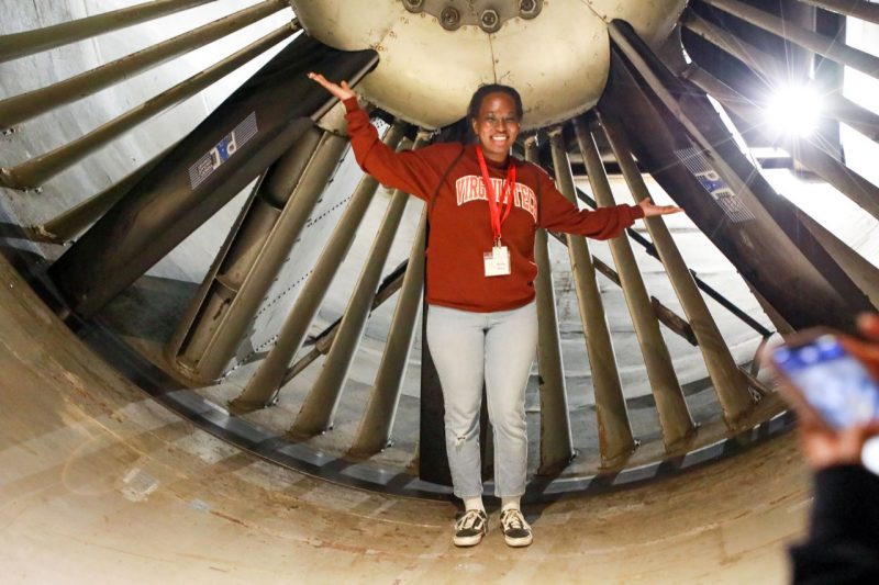 Student poses in front of the wind tunnel fans