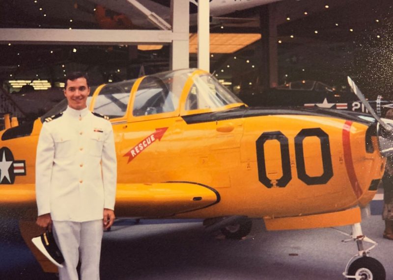 David Penberthy stands in front of a yellow plane in a Navy uniform