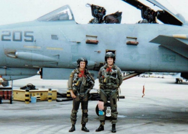 David Penberthy and a colleague stand in front of a plane in a Navy flight suit