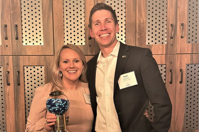 Lindsey and Matt Wildman smile at the camera while Lindsey holds her ICONS Young Professionals Award