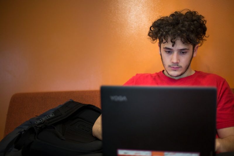 Male student sitting on a couch on a laptop.