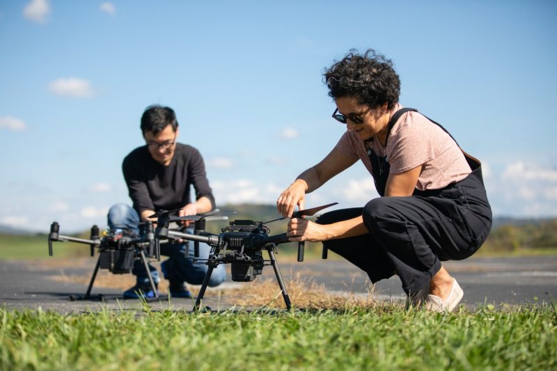 Two people working on taking apart drones outside.
