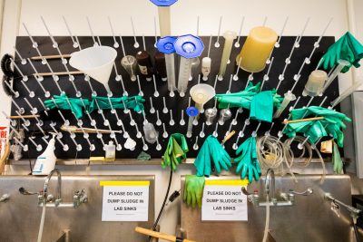 A peg board loaded with beakers and green rubber gloves. 