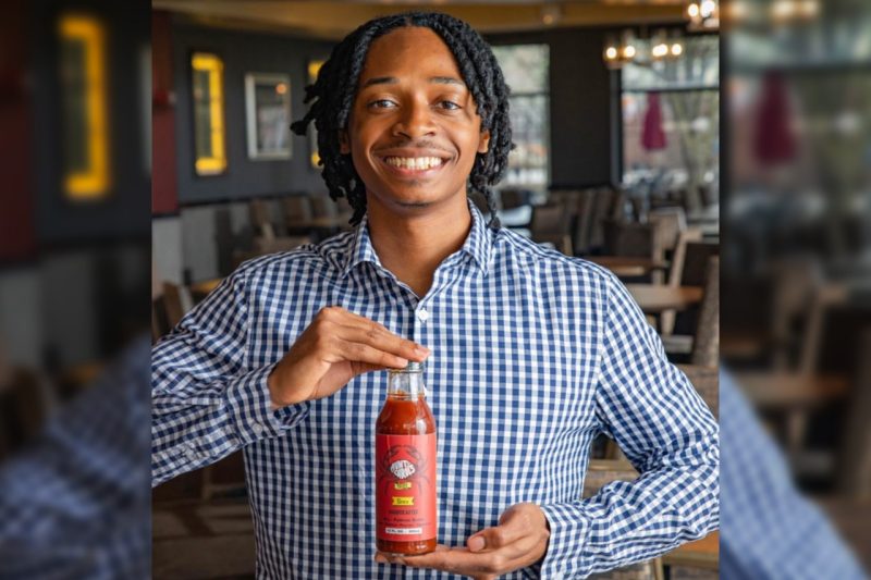 Tahjere Lewis holding up a bottle of his hot sauce.
