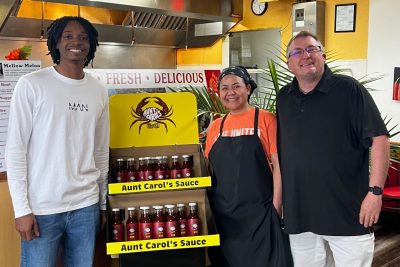 Tahjere Lewis standing in front of a display of his sauces with customers.