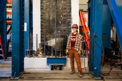 A student stands in front of a vertical concrete test wall in the Structures Lab.