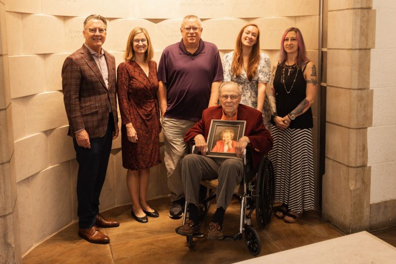 Ray Frith hold a photo of his wife while he is sitting in a wheelchair surrounded by five other people. 
