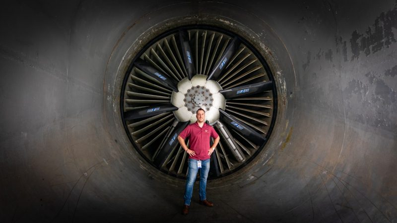 An alumni stands in front of the fan in the wind tunnel.