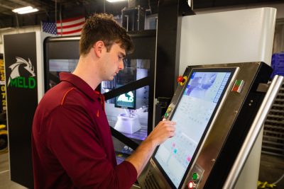A student researcher at the control panel of a 3D metal printer.