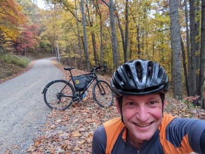 Aaron Goldstein takes a selfie with his bike on a fall foliage gravel road.