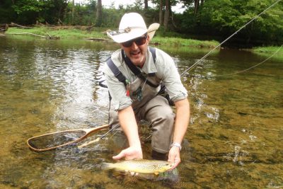 Angelo Biviano holds a trout for a photo while in a river.