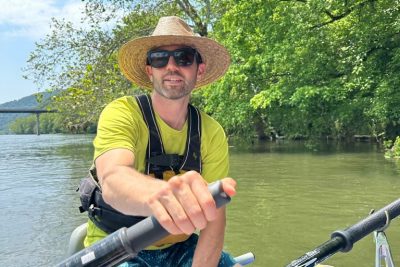 Close up of Tripp Shealy paddling a raft on a peaceful river.