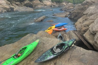 Kayaks resting on large rocks along a river with rapids.