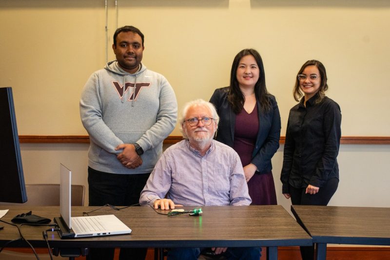 The team of three researchers and the test subject pose behind a table for a group photo.