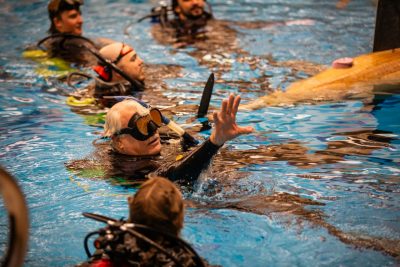 Chuck Swecker, talks with team members in the pool, all in scuba gear.