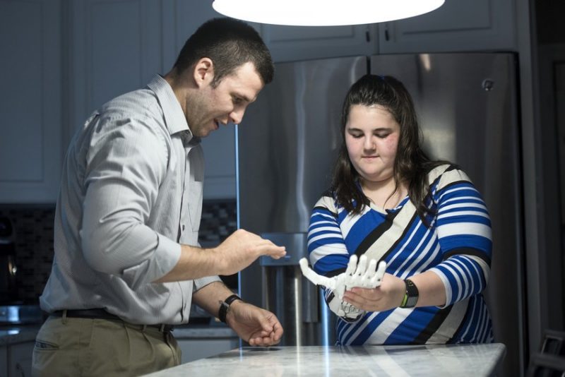 Josie tries on the prosthetic hand as Blake Johnson offers guidance. They're situated in Josie's kitchen.