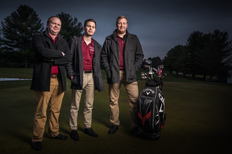 Jacob Fallon, Eric Gilmer, and Any Cohen pose for a group portrait on the golf course in the late evening.