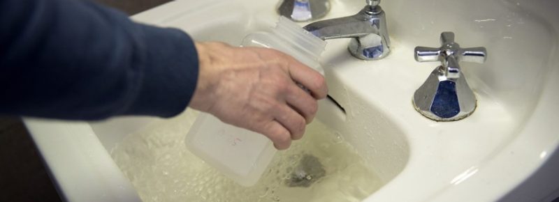 A person fills up a plastic bottle in a sink that is filled with brown water.
