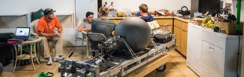A Hyperloop pod sits in the garage of the Airbnb where the Hyperloop team stayed in California. Multiple members of the team sit around the pod.