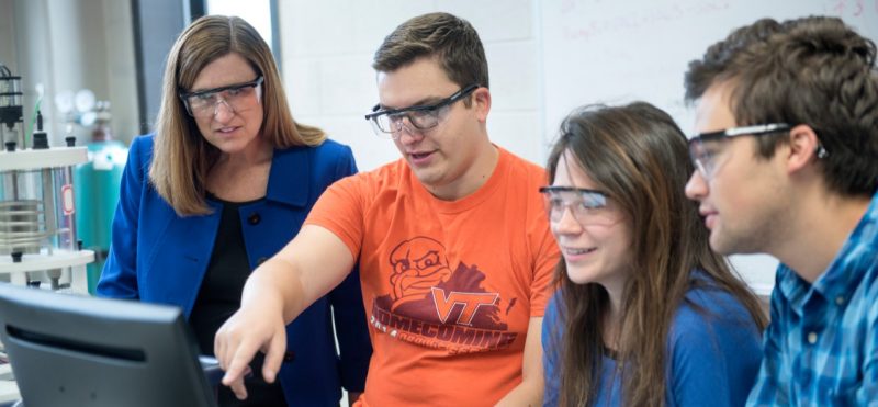 Three Virginia Tech students are pointing to a screen and explaining some research to Dean Ross