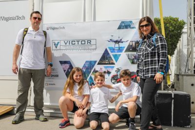 Three kids and two adults posting in front of a Team VICTOR banner